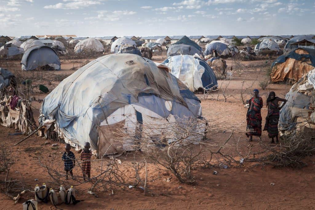Des femmes et enfants devant une multitude de tentes et de hangars