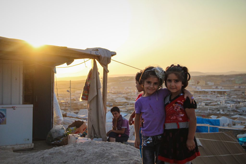 Des enfants sourient en regardant l'objectif devant un coucher de soleil sur le camp